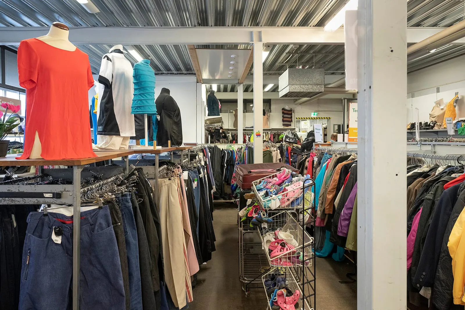 Racks of secondhand clothing, shoes and mannequins on the shop floor of a large reuse centre