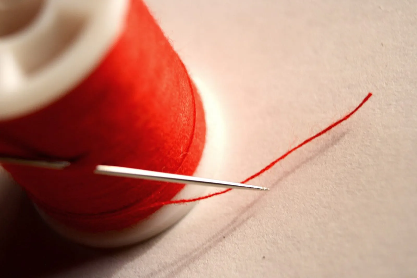 A spool of red thread with a needle resting on white fabric