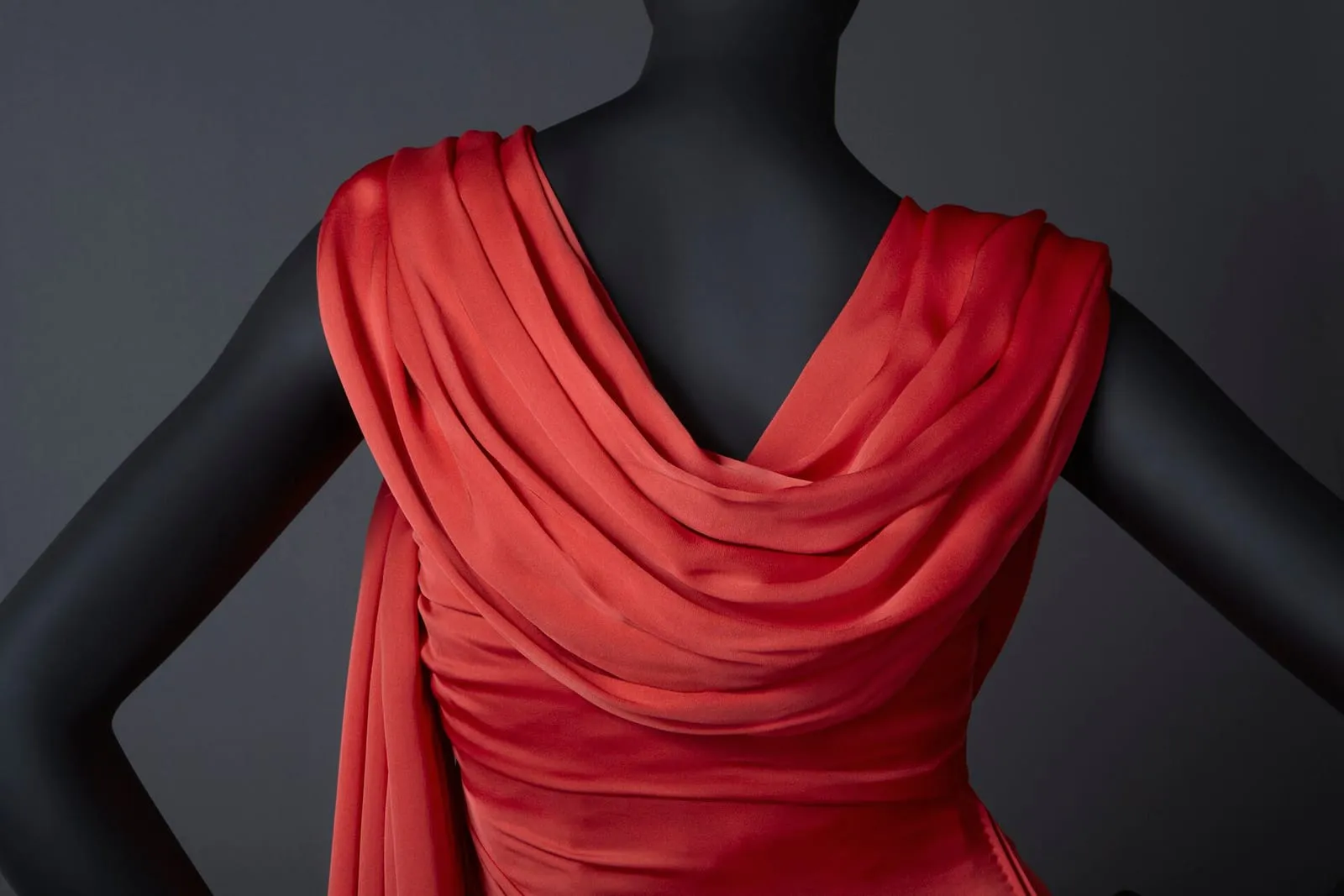 A draped red silk evening gown pinned on a black display mannequin