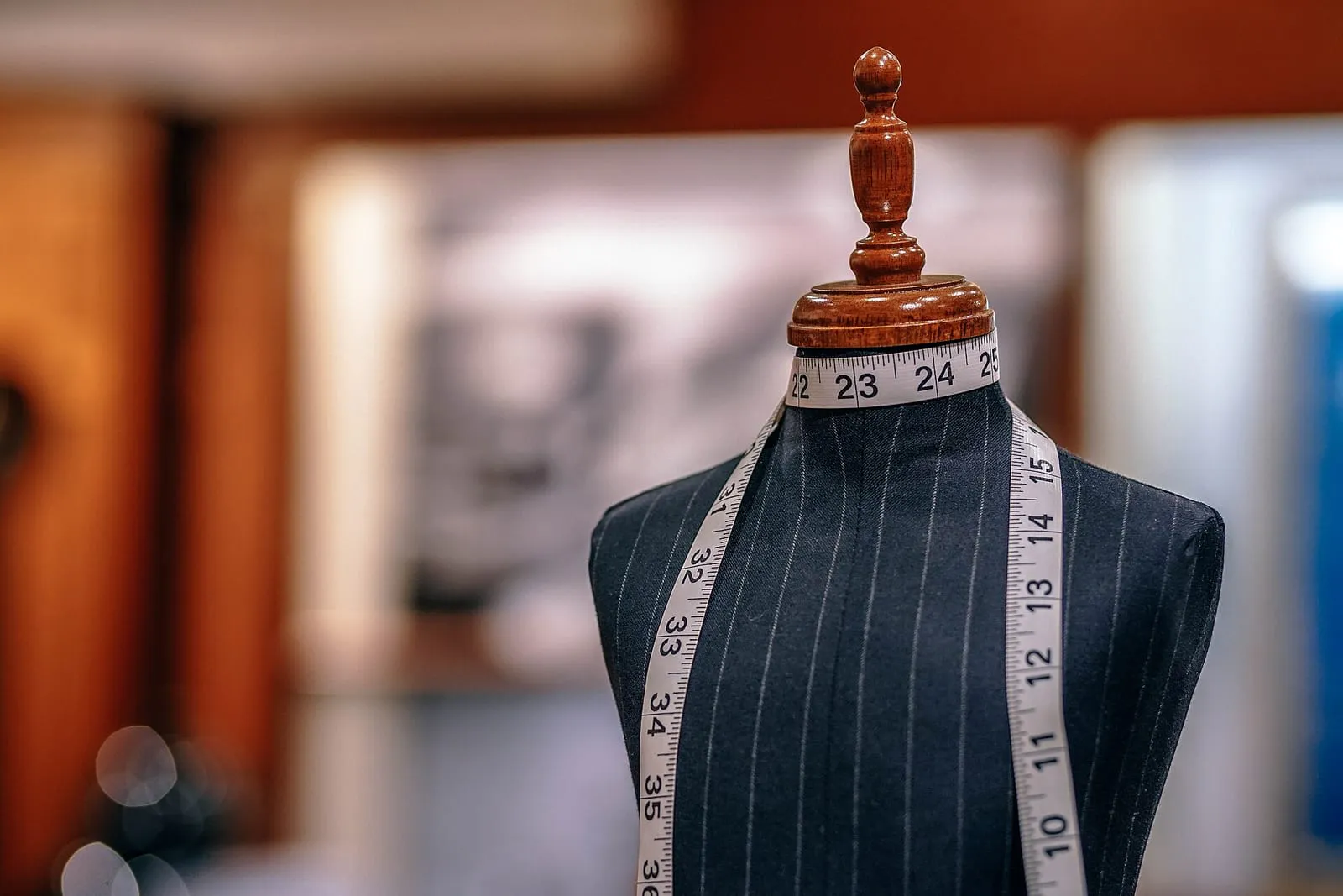A tailor's dress form in a pinstriped garment with a tape measure draped over its shoulders