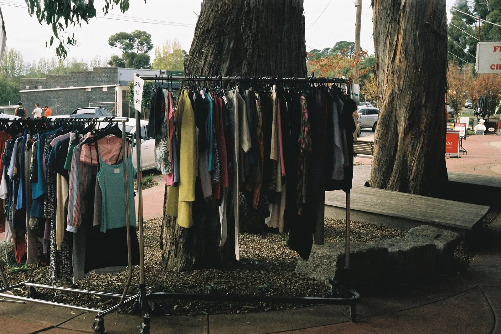 A rail of secondhand clothes standing outdoors beside a roadside stall